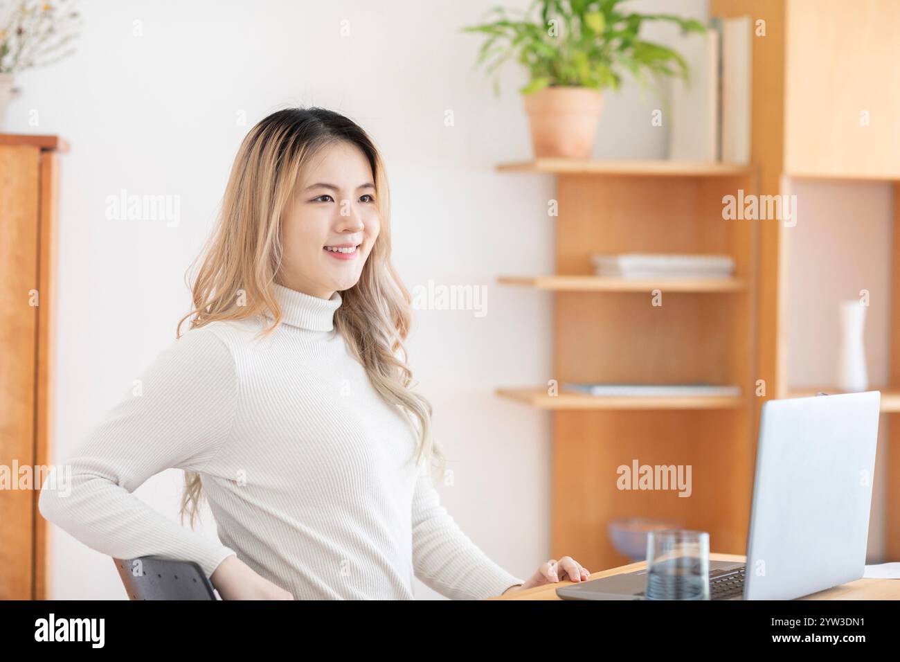 Giovane donna sorridente seduta di fronte a un notebook in un ambiente di ufficio luminoso. Foto Stock