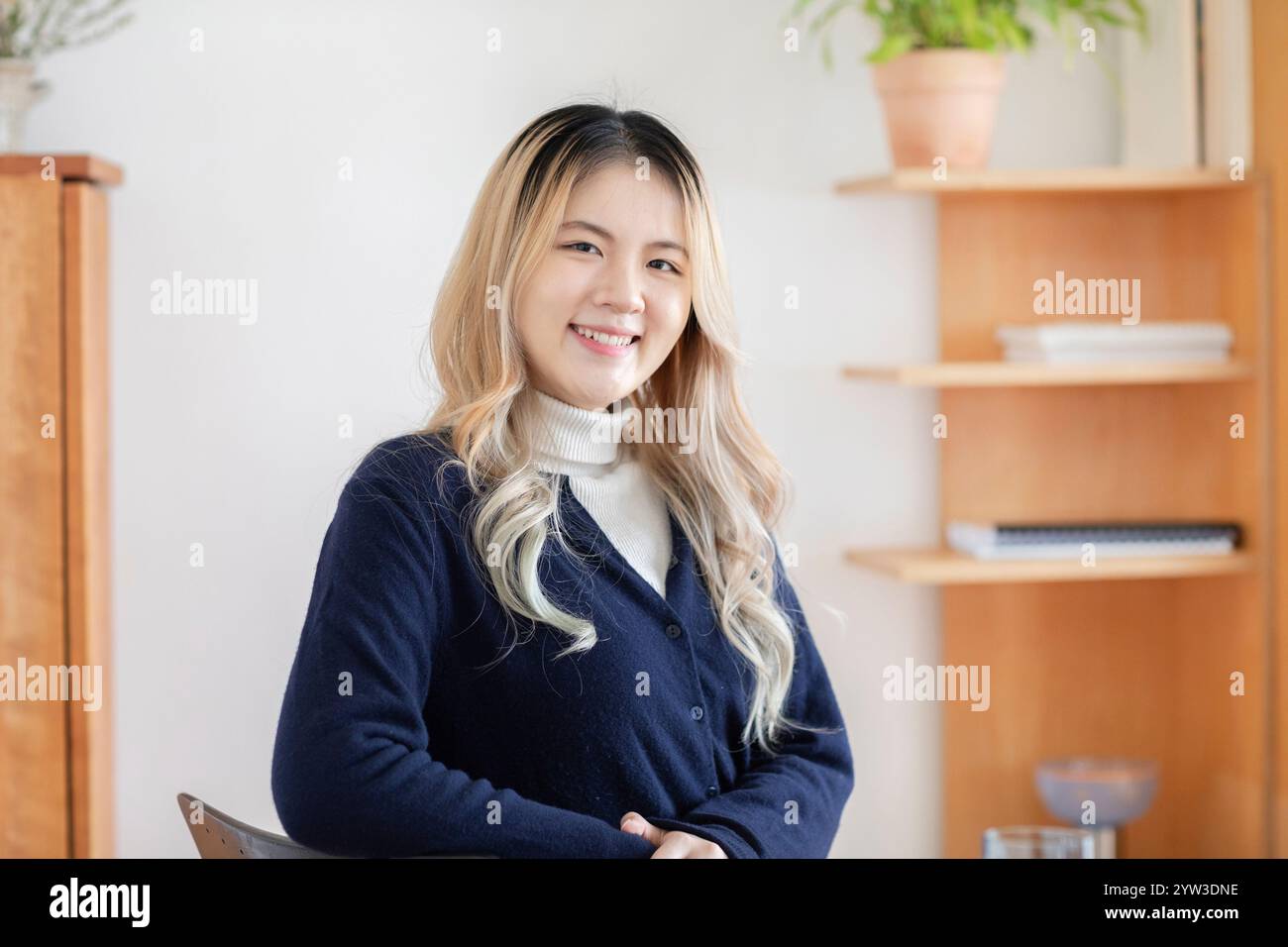 Giovane donna sorridente con luci bionde in una stanza ben illuminata con scaffali sullo sfondo. Foto Stock