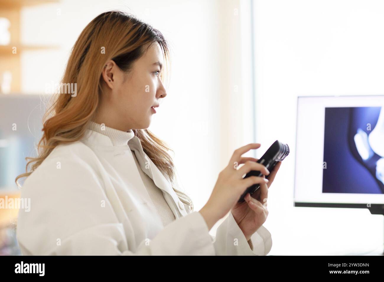 Una donna professionista esamina una fotocamera in un ufficio illuminato con lo schermo di un computer sullo sfondo. Foto Stock