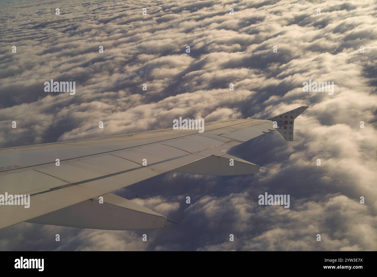 Ali di aeroplano che si innalzano sopra un denso strato di nuvole durante l'alba dorata Foto Stock