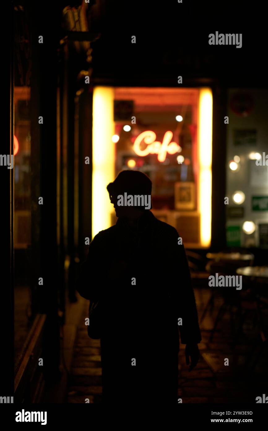 Figura sagomata in piedi di fronte a un bar illuminato di notte Foto Stock