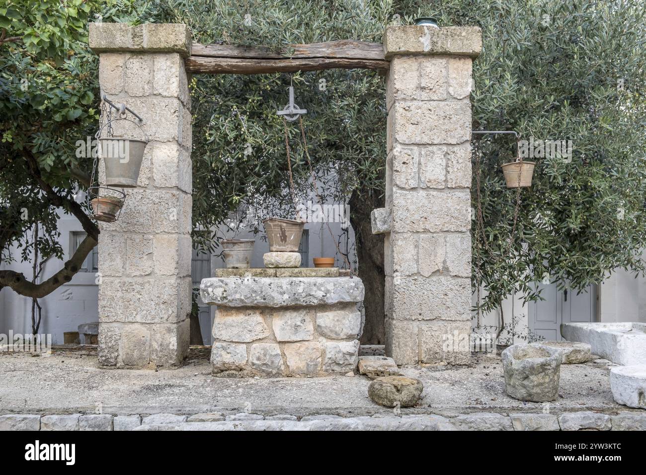 Vecchia fontana in pietra in un giardino mediterraneo con secchi e corde, circondata da alberi, Puglia, Italia, Europa Foto Stock