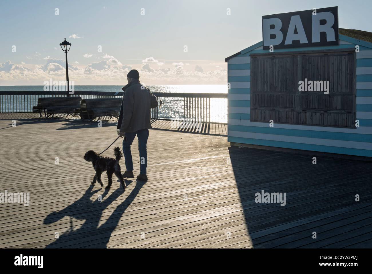 Camminatore di cani sul molo di Hastings nel soleggiato pomeriggio invernale, Hastings, East Sussex, Inghilterra, Regno Unito, Europa Foto Stock