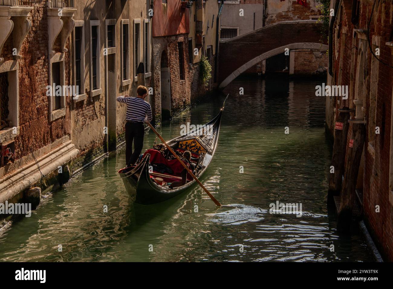 Venezia classica per i turisti: Una gondola trainata da un gondoliere in uno dei tanti canali più piccoli, i cosiddetti "rios", che attraversano il centro storico. A causa della costante umidità, la maggior parte dei vecchi edifici hanno un aspetto piuttosto romantico, a volte morboso. Il centro storico di Venezia è patrimonio dell'umanità dell'UNESCO. Foto Stock