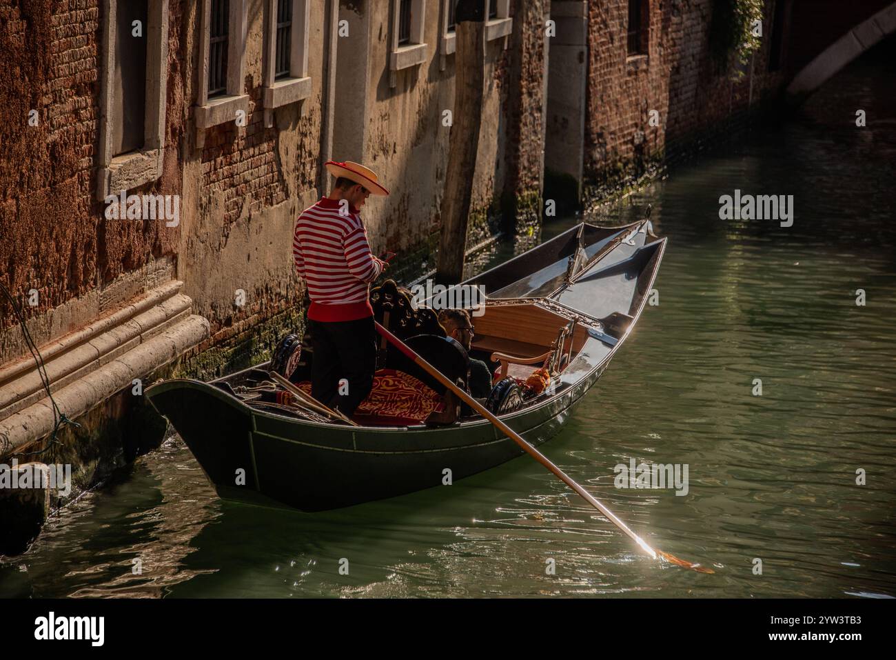 Venezia classica per i turisti: Una gondola trainata da un gondoliere in uno dei tanti canali più piccoli, i cosiddetti "rios", che attraversano il centro storico. A causa della costante umidità, la maggior parte dei vecchi edifici hanno un aspetto piuttosto romantico, a volte morboso. Il centro storico di Venezia è patrimonio dell'umanità dell'UNESCO. Foto Stock