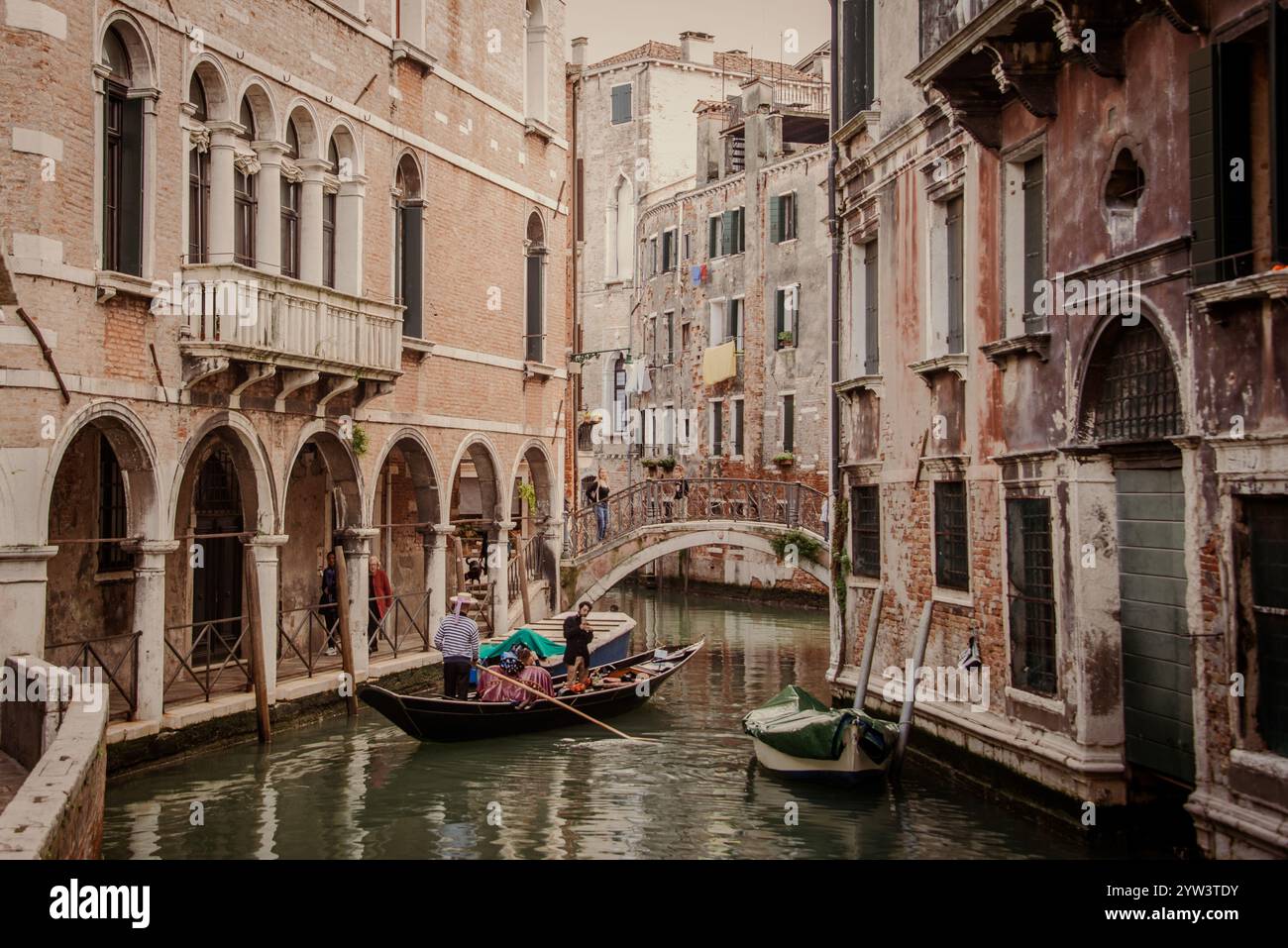 Venezia classica per i turisti: Una gondola trainata da un gondoliere in uno dei tanti canali più piccoli, i cosiddetti "rios", che attraversano il centro storico. A causa della costante umidità, la maggior parte dei vecchi edifici hanno un aspetto piuttosto romantico, a volte morboso. Il centro storico di Venezia è patrimonio dell'umanità dell'UNESCO. Foto Stock