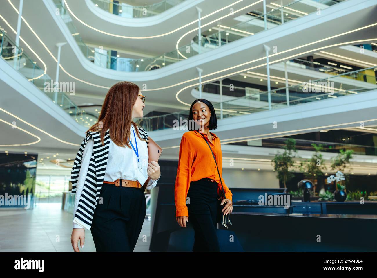 Due donne professionali che conversano in un ambiente aziendale contemporaneo, evidenziando la crescita della carriera nel settore finanziario. Foto Stock