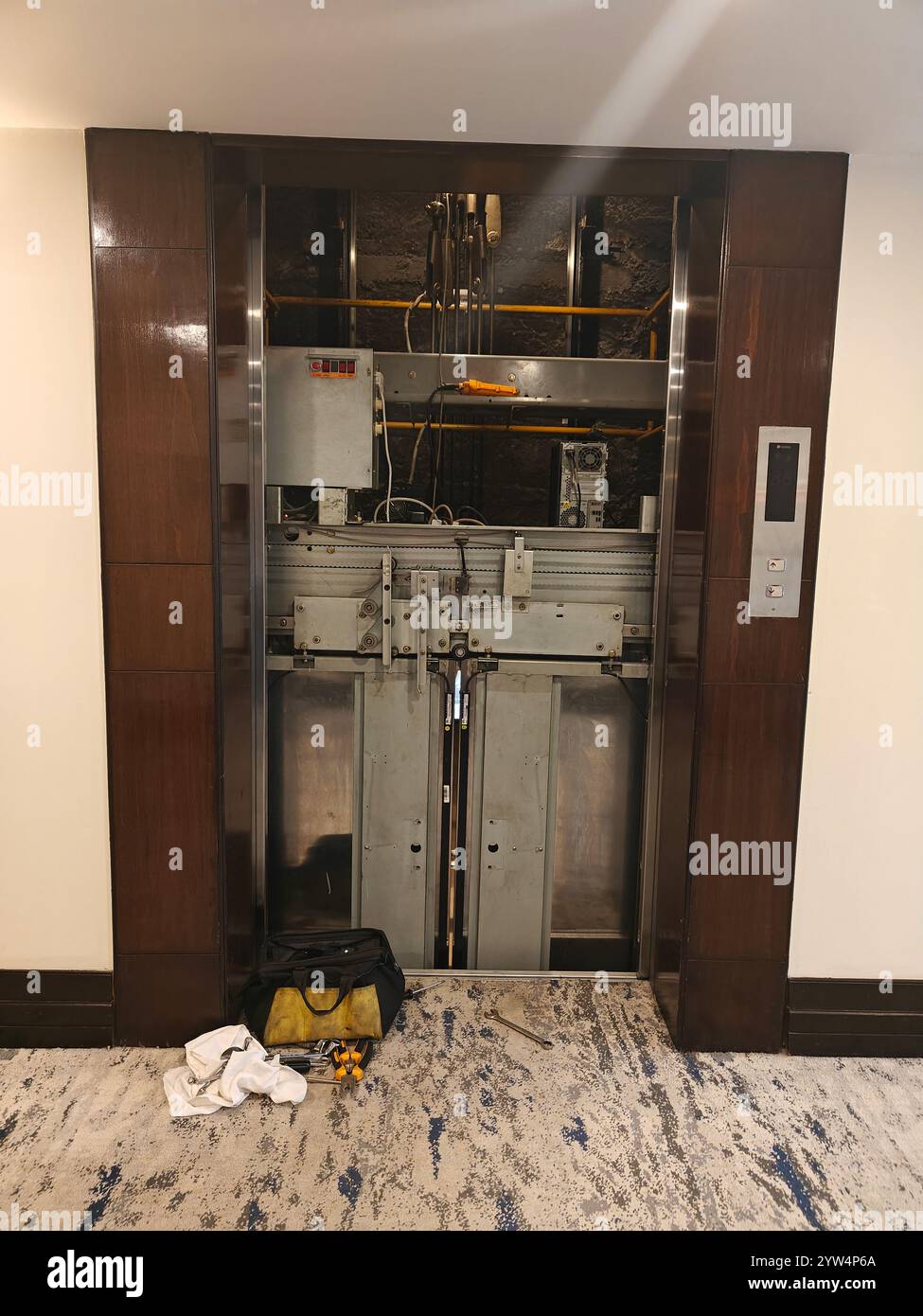 Il personale addetto alla manutenzione sta lavorando su un sistema di ascensori in un corridoio dell'hotel con attrezzi e attrezzature nelle vicinanze. Foto Stock