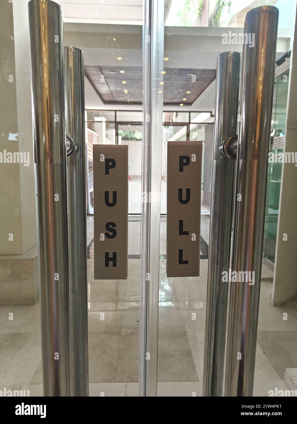 La segnaletica sulle porte di vetro fornisce istruzioni chiare per entrare in un edificio moderno in una trafficata area urbana. Foto Stock