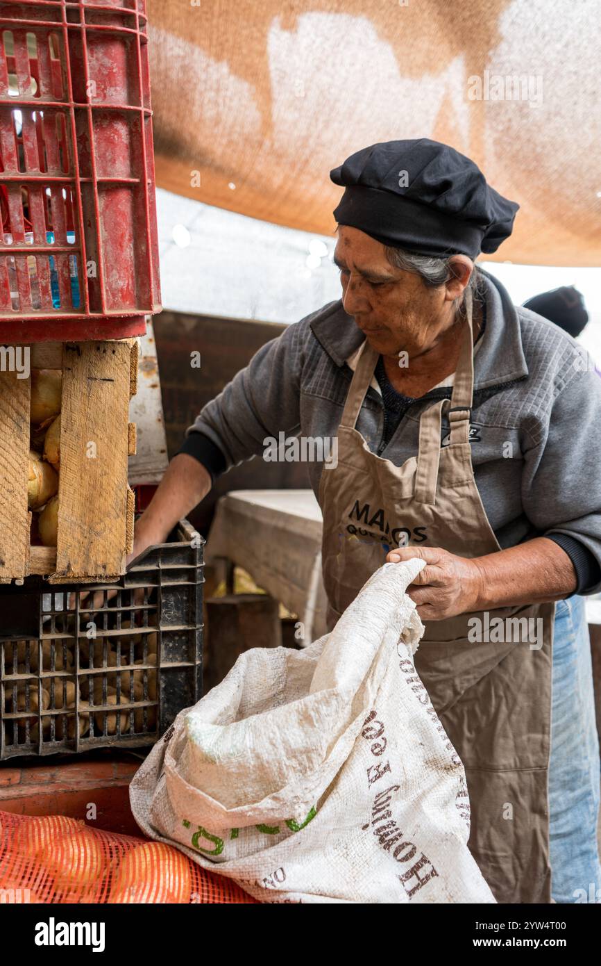Lurin, Lima, Perù - 6 settembre 2024: Una donna più anziana che indossa un cappello da cucina nero afferra le patate e le mette in un sacco bianco per la conservazione in the Comm Foto Stock