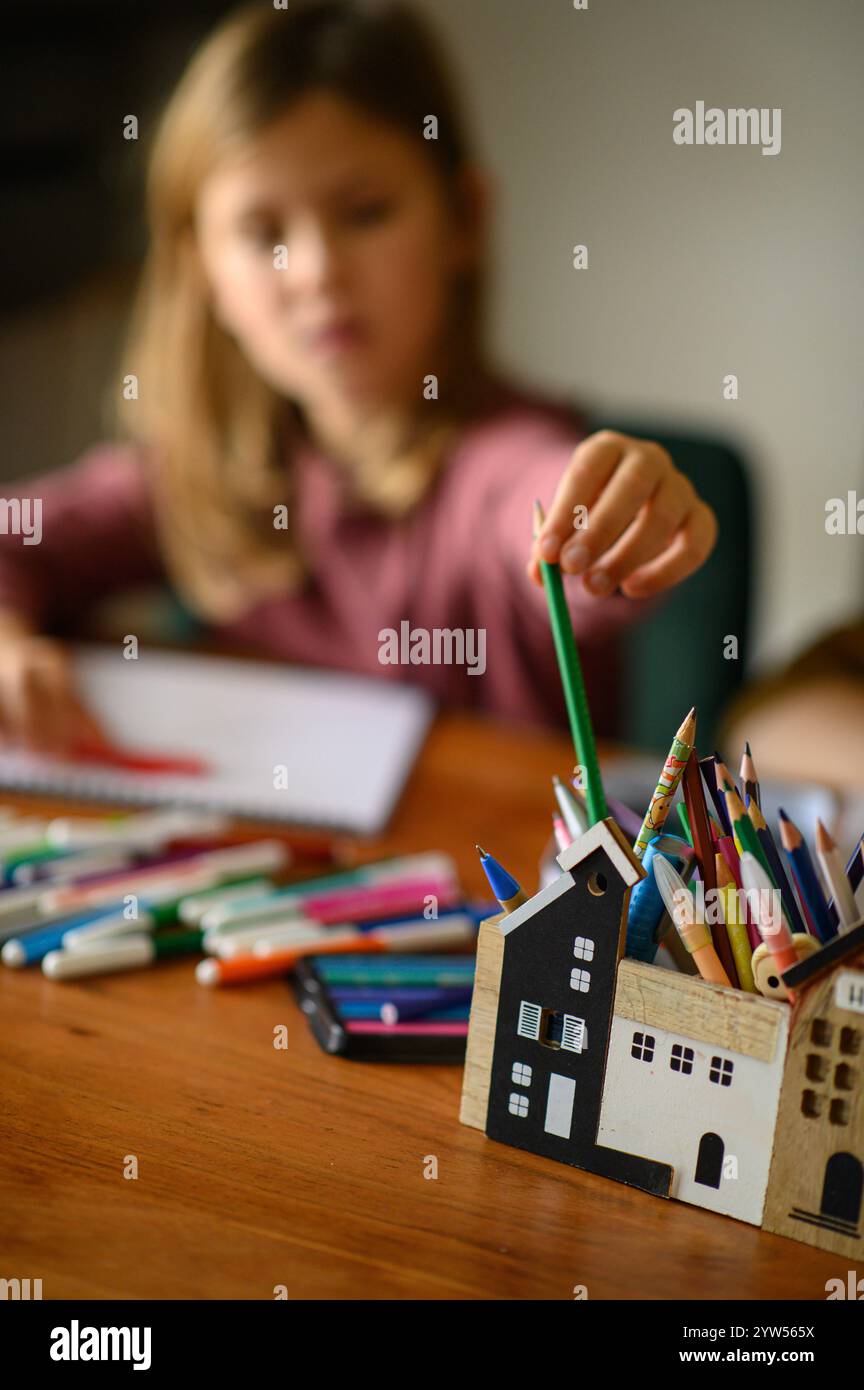 la ragazza è seduta sul tavolo che sta studiando pittura e lettura con molti pennarelli e matite intorno Foto Stock