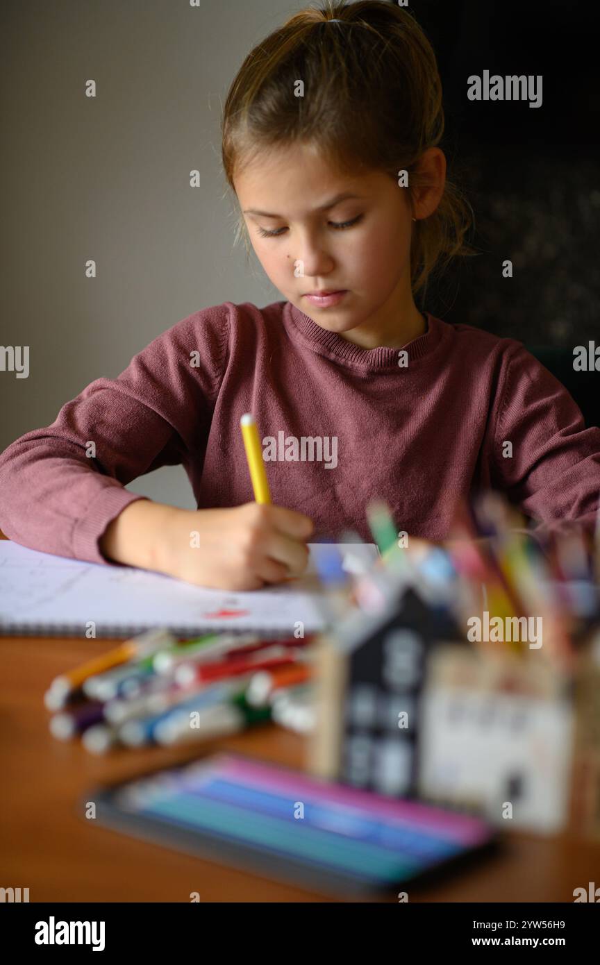 la ragazza è seduta sul tavolo che sta studiando pittura e lettura con molti pennarelli e matite intorno Foto Stock