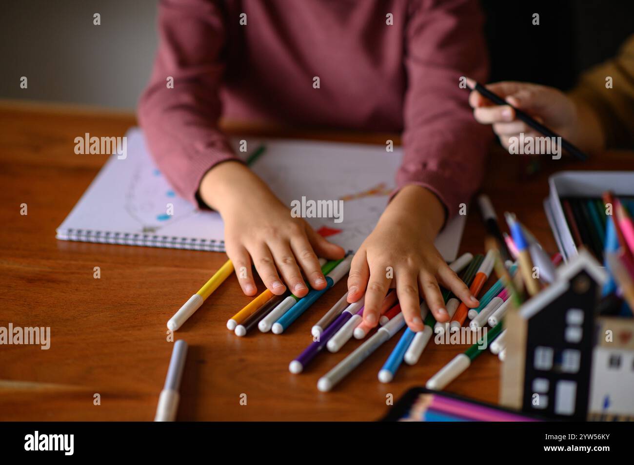la ragazza è seduta sul tavolo che sta studiando pittura e lettura con molti pennarelli e matite intorno Foto Stock