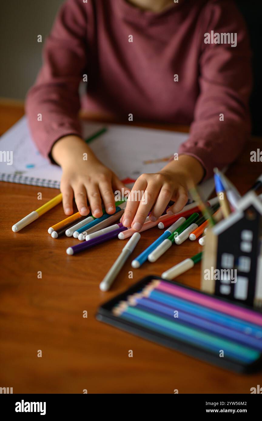 la ragazza è seduta sul tavolo che sta studiando pittura e lettura con molti pennarelli e matite intorno Foto Stock