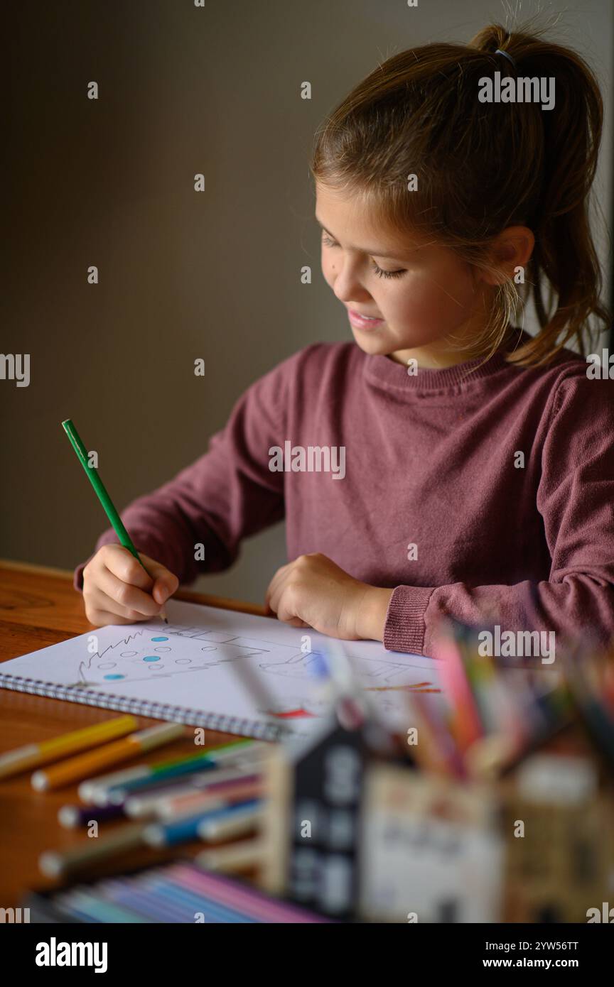 la ragazza è seduta sul tavolo che sta studiando pittura e lettura con molti pennarelli e matite intorno Foto Stock