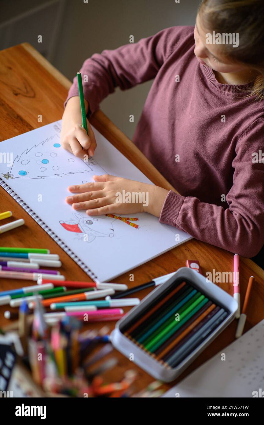 la ragazza è seduta sul tavolo che sta studiando pittura e lettura con molti pennarelli e matite intorno Foto Stock