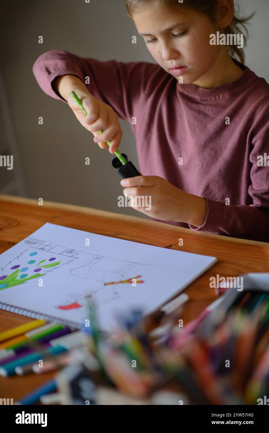 la ragazza è seduta sul tavolo che sta studiando pittura e lettura con molti pennarelli e matite intorno Foto Stock