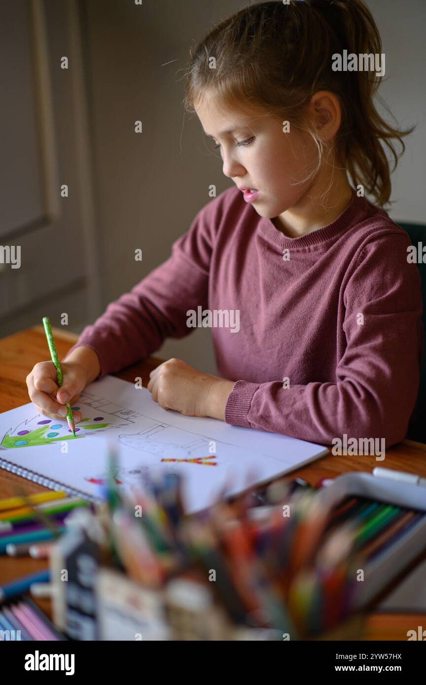 la ragazza è seduta sul tavolo che sta studiando pittura e lettura con molti pennarelli e matite intorno Foto Stock