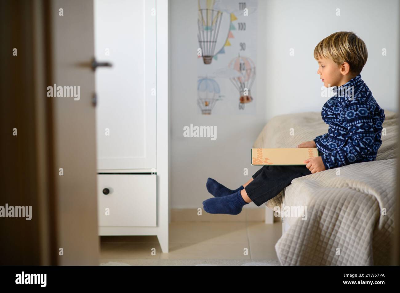 Il bambino è seduto sul letto in una stanza dei bambini e sta leggendo libri Foto Stock