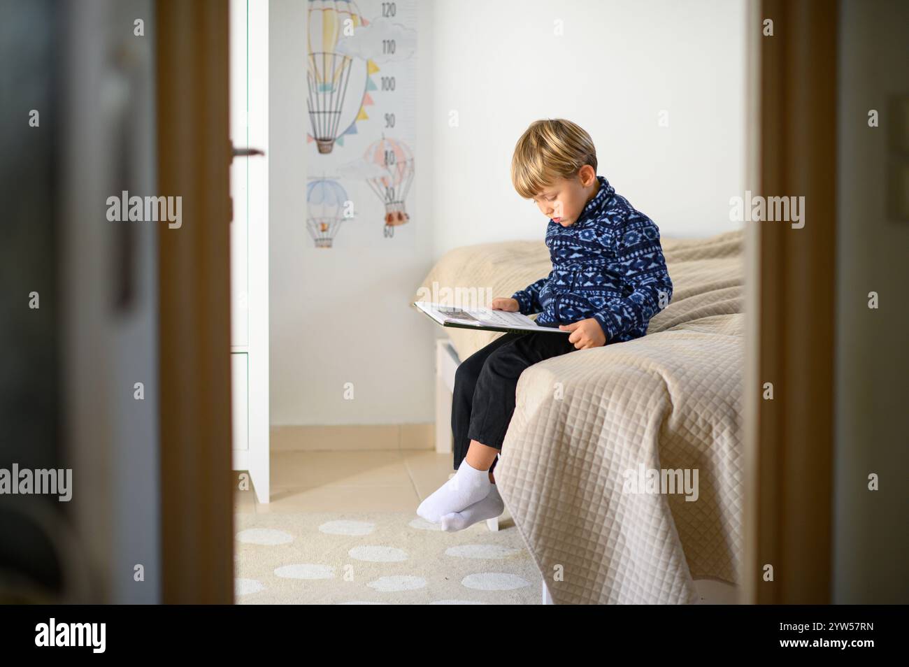 Il bambino è seduto sul letto in una stanza dei bambini e sta leggendo libri Foto Stock