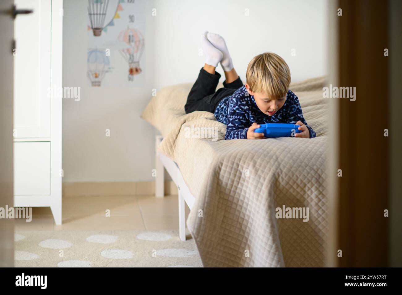 un ragazzo è sdraiato su un letto in una stanza dei bambini e gioca ai videogiochi Foto Stock