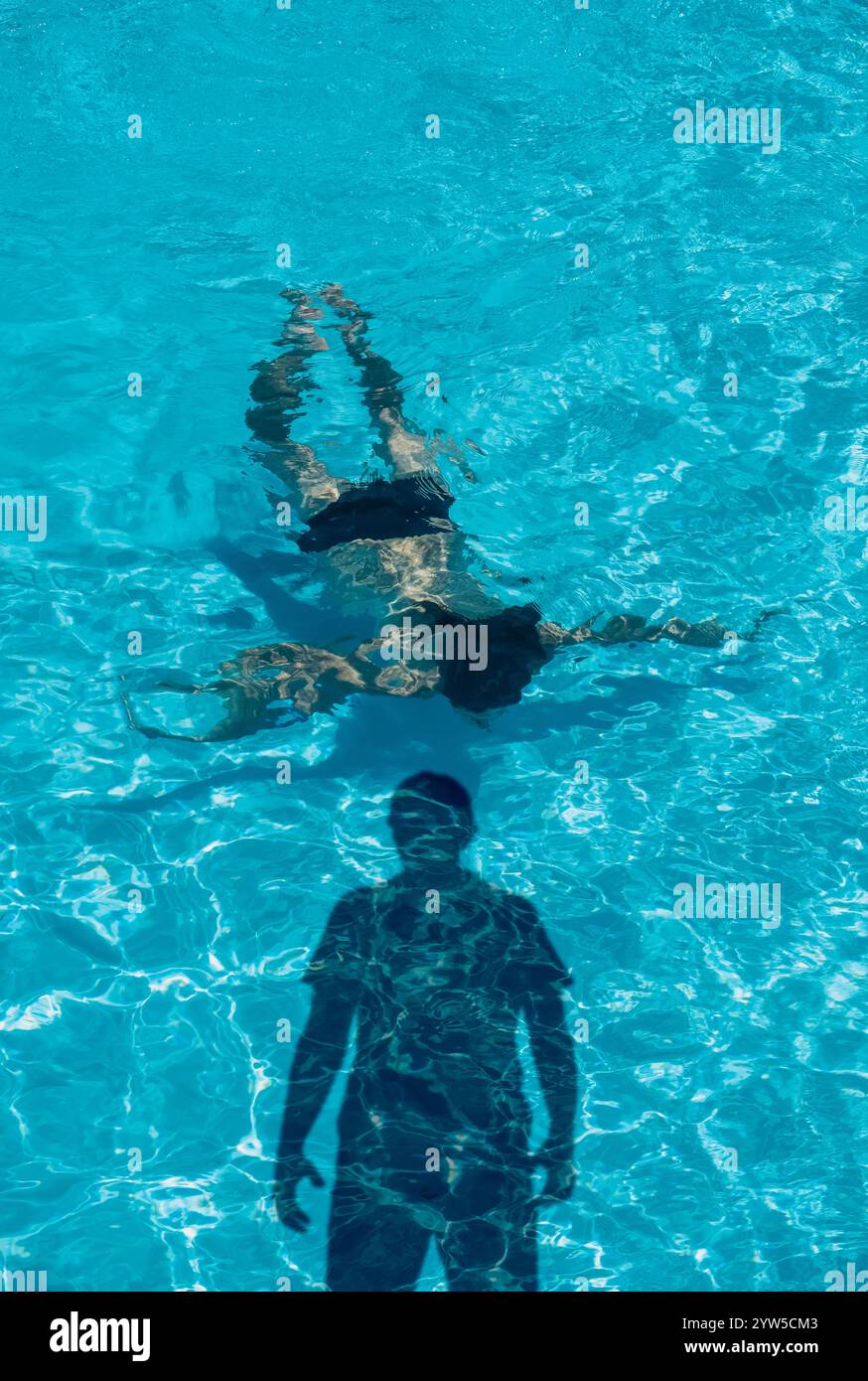 Donna a faccia in giù in piscina con la sinistra ombra dell'uomo Foto Stock
