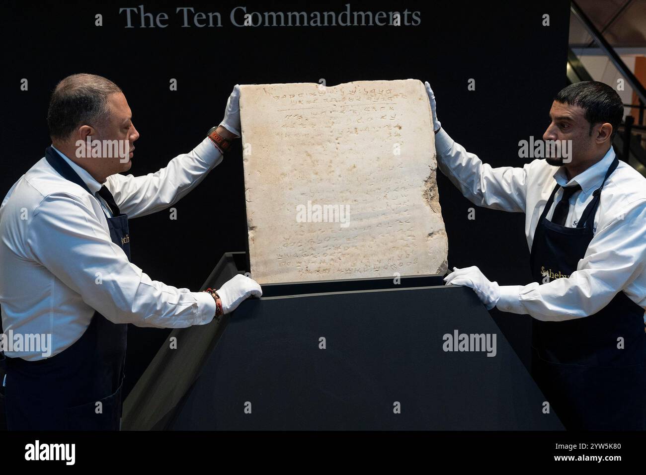 New York, New York, Stati Uniti. 9 dicembre 2024. I lavoratori tengono in attesa durante l'anteprima della stampa la più antica tavoletta scritta dei dieci comandamenti risalente alla tarda epoca romano-bizantina (ca. 300-800 d.C.) da mettere all'asta come singolo lotto più tardi a dicembre presso la casa d'aste Sotheby's a New York il 9 dicembre 2024. Questo tablet è l'unico esempio completo conosciuto del suo genere. Tavoletta di marmo incisa in alfabeto paleo-ebraico e fu scavata nella costa meridionale di Israelin 1913 vicino ai siti delle prime sinagoghe, chiese e moschee. (Credit Image: © Lev Radin/ZUMA Press Wire) SOLO PER USO EDITORIALE! Non per Commer Foto Stock