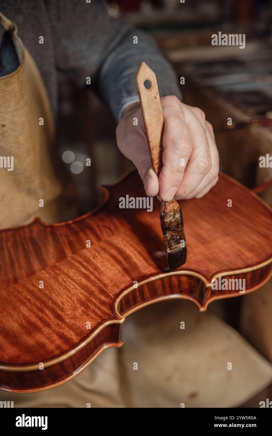 Luthier applica con cura la vernice su un violino artigianale nella sua bottega, mettendo in mostra la tradizione artigianale italiana Foto Stock