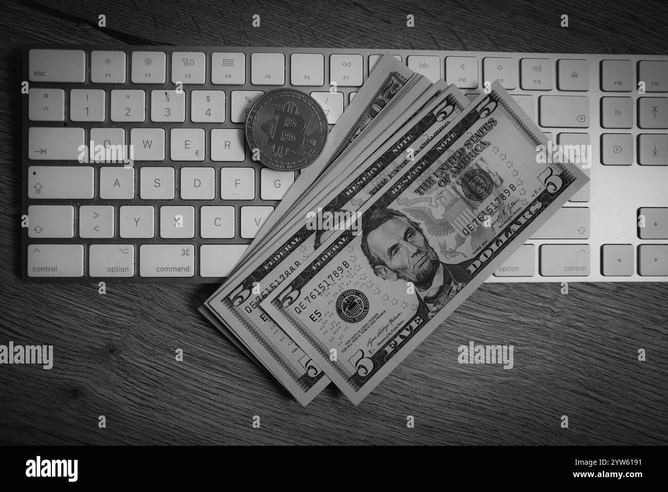 Una moneta Bitcoin si trova sulla scrivania accanto a qualche banconota da un dollaro sulla tastiera di un computer Foto Stock