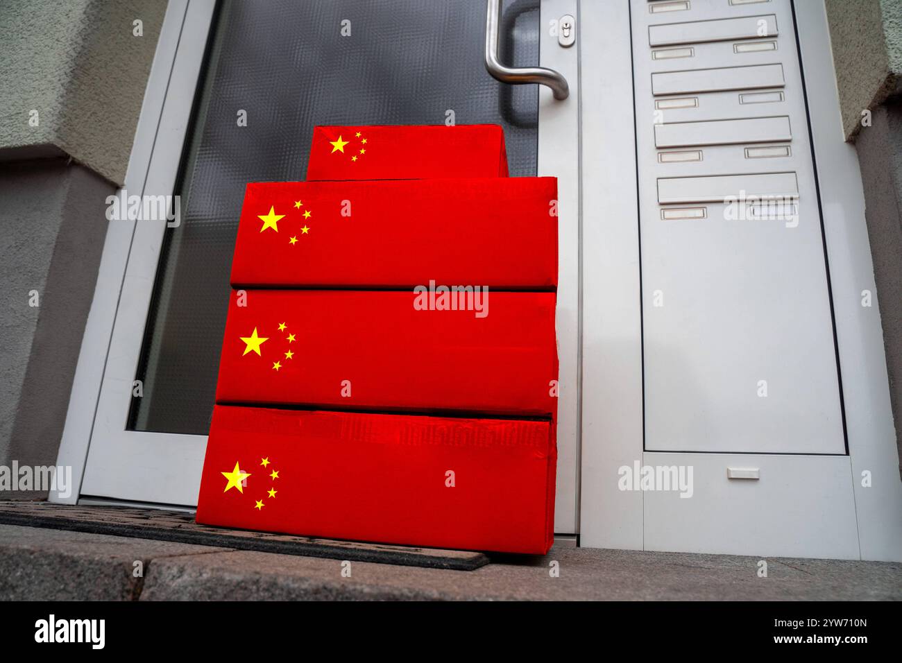 Baviera, Germania - 9 dicembre 2024: Pacchi con bandiera cinese sul gradino della porta rappresentano il fiorente commercio di merci dalla Cina. Il simbolo dei prodotti asiatici domina il mercato internazionale, ma le tariffe punitive, le critiche ambientali e le condizioni di lavoro stanno diventando sempre più problemi nella politica e nella società. Il dibattito sulle pratiche commerciali eque, la sostenibilità e la dipendenza dalla Cina si sta intensificando in tempi di incertezza globale. FOTOMONTAGGIO *** Pakete mit chinesischer Flagge vor einer Haustür stehen für den boomenden Handel mit Waren aus China. Symbol für Produkte aus dem Foto Stock
