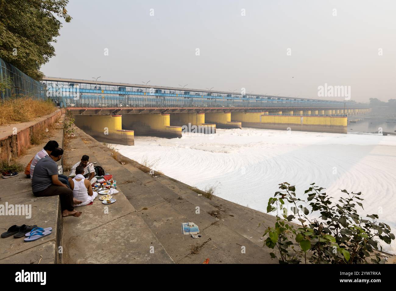 le persone che eseguono l'ultimo rituale di rito vicino al fiume inquinato con schiuma tossica e ponte stradale al mattino l'immagine viene scattata presso il fiume yamuna okhla sbarrage delhi i Foto Stock