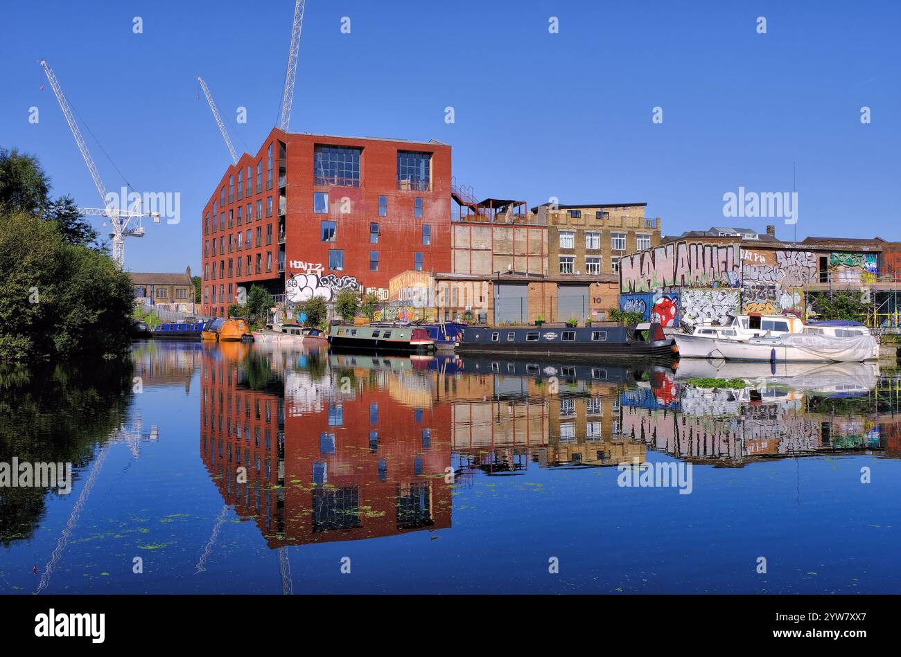 Graffiti colorati, barche sul canale, chiatte, gru a torre ed edifici con riflessi a specchio sulla navigazione sul fiume Lee a Stratford, Londra, Inghilterra, Regno Unito Foto Stock