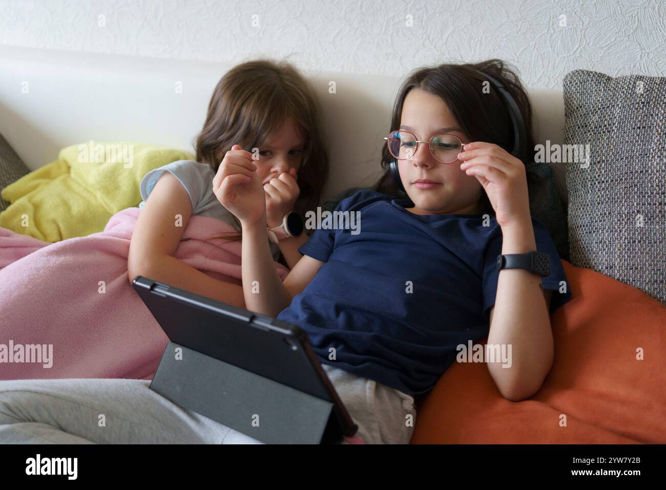 Due sorelle sdraiate sul divano che guardano la tavoletta. Concetto di bambini che trascorrono del tempo a casa Foto Stock