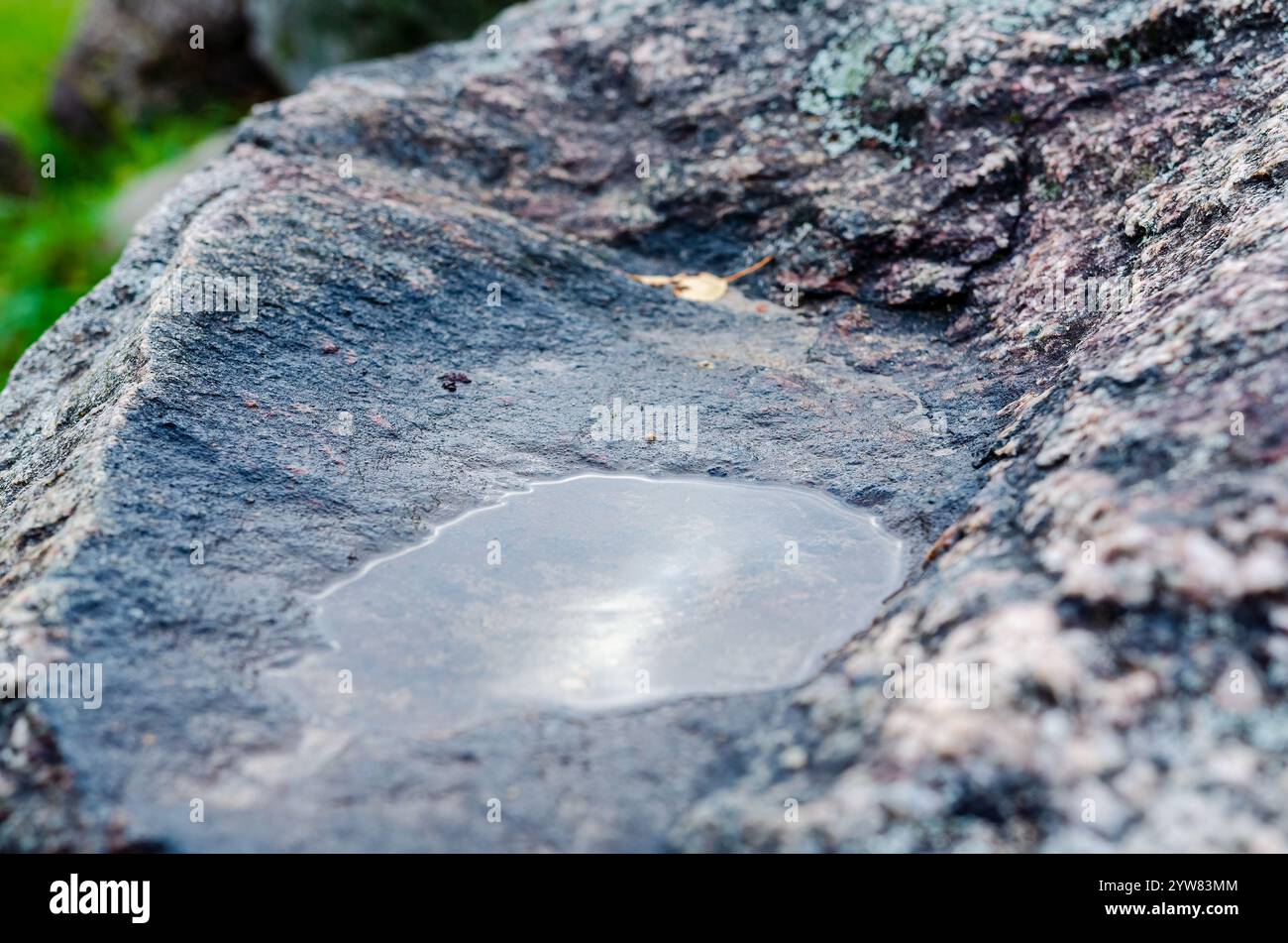 Pozzetto d'acqua poco profondo su superfici in pietra ruvida. Calma, atmosfera serena, angolo macro, posizione bassa, ambiente naturale all'aperto, concentrati sulla struttura, geologica Foto Stock