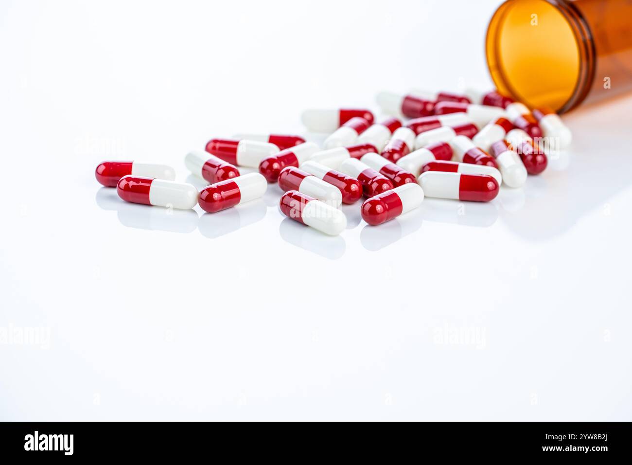 Capsule di prescrizione rosse e bianche che fuoriescono da un contenitore di plastica. Farmaci farmaceutici regolamentati. Enfatizzare gli standard di sicurezza, i farmaci Foto Stock