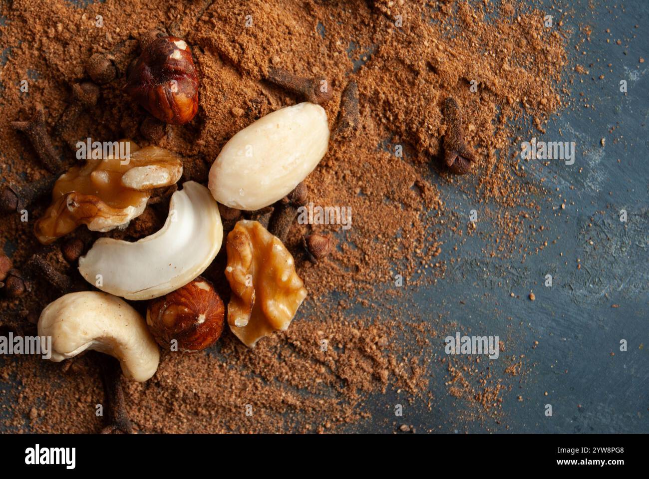 Un mix di noci, mandorle e nocciole posto su una cannella macinata su uno sfondo rustico. Foto Stock