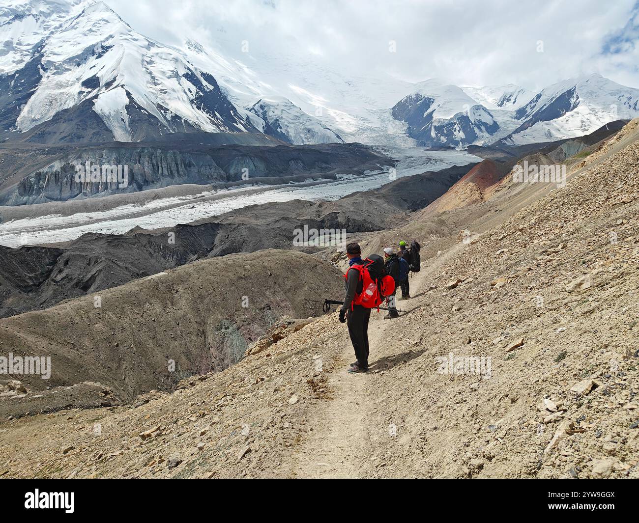 Gli avventurieri attraversano un sentiero accidentato, circondato da montagne maestose e viste glaciali durante il loro viaggio di trekking. Foto Stock