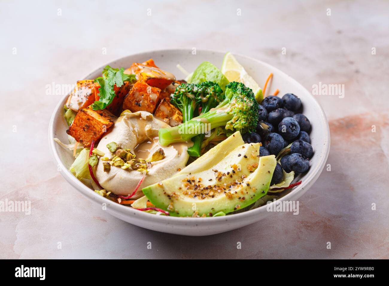 Ciotola per pranzo vegan bilanciata con patate dolci al forno, avocado, frutti di bosco, insalata e hummus. Concetto di dieta basata sulle piante. Foto Stock