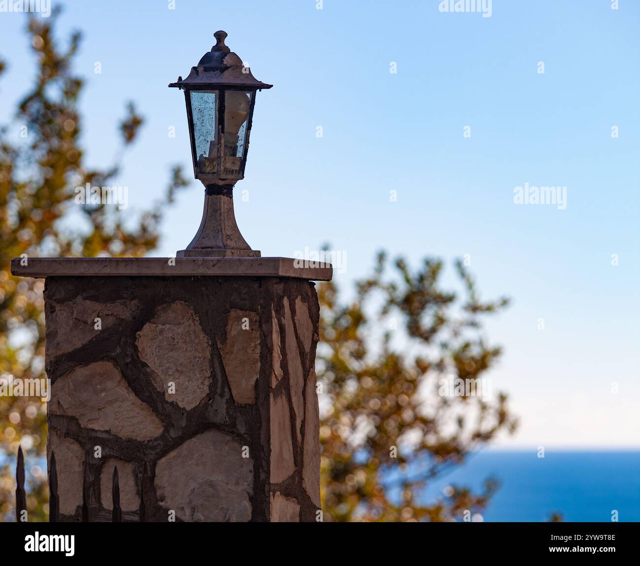 Lampada piccola su un montante di pietra. Sullo sfondo un albero e un mare blu. Foto di alta qualità. Foto Stock