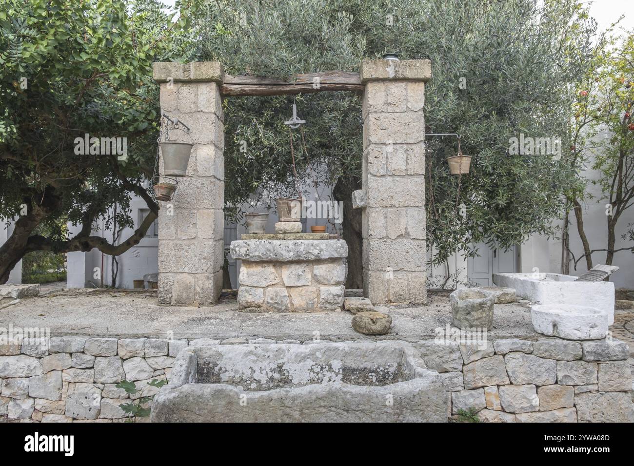 Un'antica fontana di pietra circondata da alberi trasmette un fascino rustico e rurale, Puglia, Italia, Europa Foto Stock