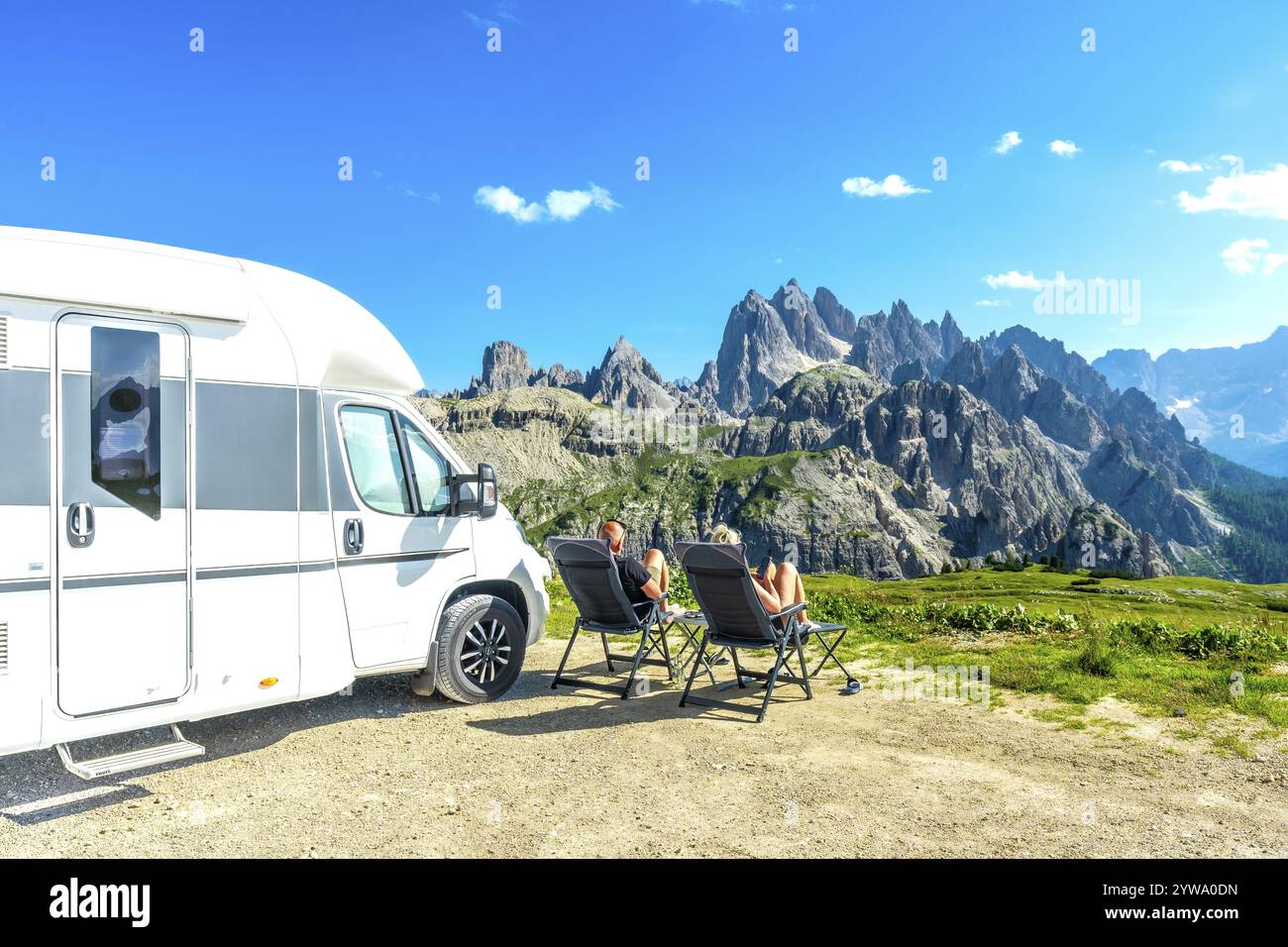 La famiglia si rilassa sulle sedie da campeggio, godendo di una vista mozzafiato sulle tre cime di lavaredo, dolomiti, italia, durante le vacanze estive con il camper Foto Stock