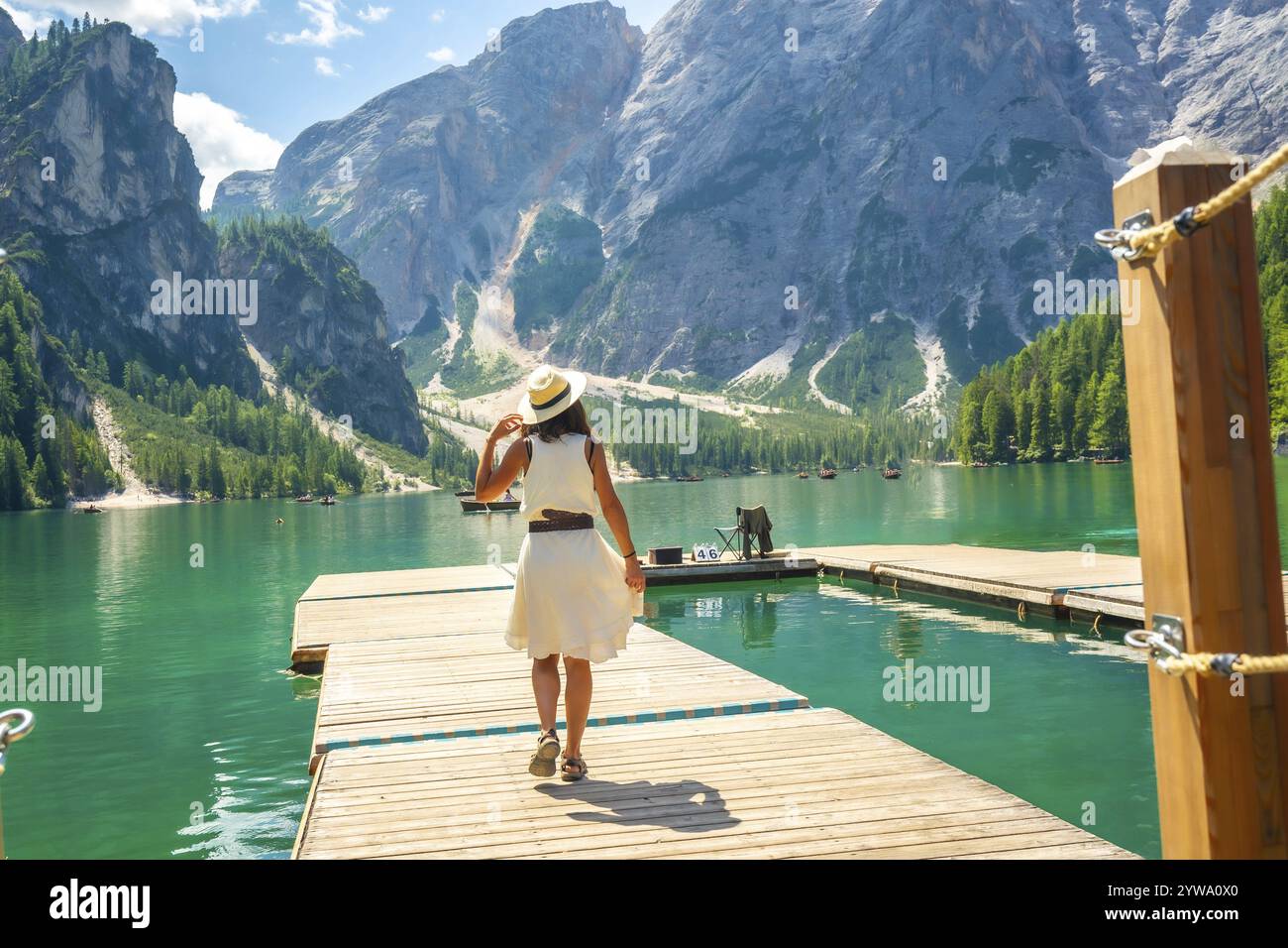 Il turista cammina su un molo di legno, ammirando la vista panoramica del lago di braies e delle montagne circostanti delle dolomiti in estate Foto Stock