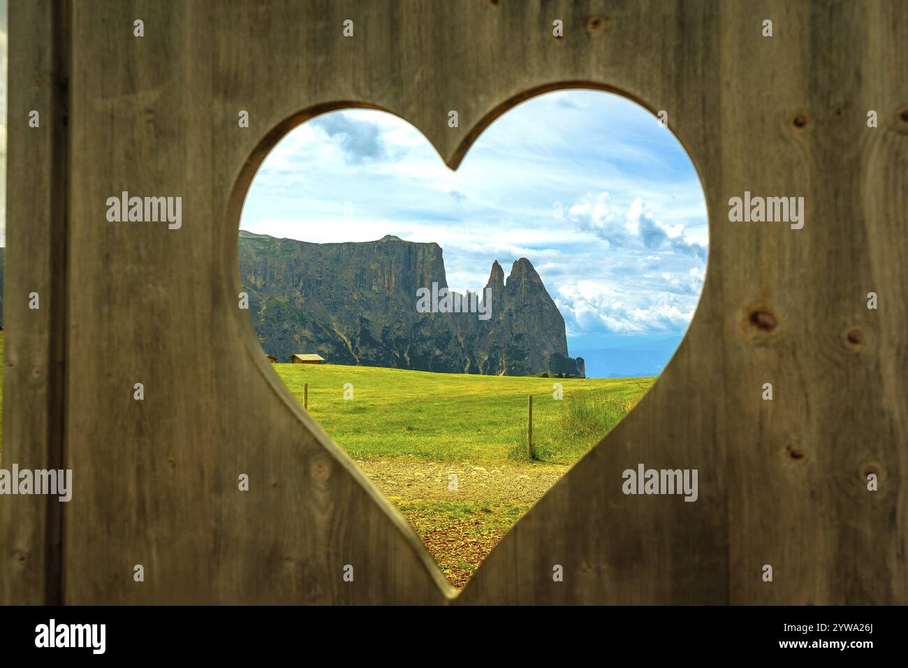 Vista mozzafiato delle dolomiti italiane, vista attraverso un'apertura a forma di cuore in una recinzione di legno, che mostra la bellezza dell'alpe di siusi Foto Stock