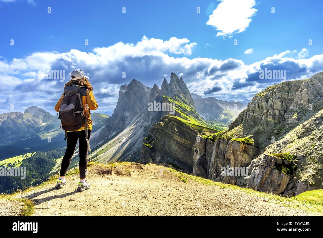 Turista donna con zaino che ammira la catena montuosa delle odle nelle dolomiti italiane in una soleggiata giornata estiva Foto Stock