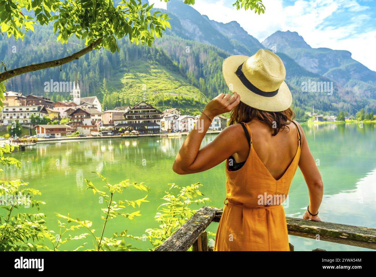 Giovane donna che indossa abiti estivi e cappello di paglia godendo di una vista mozzafiato del villaggio di alleghe e del suo lago nelle dolomiti italiane Foto Stock