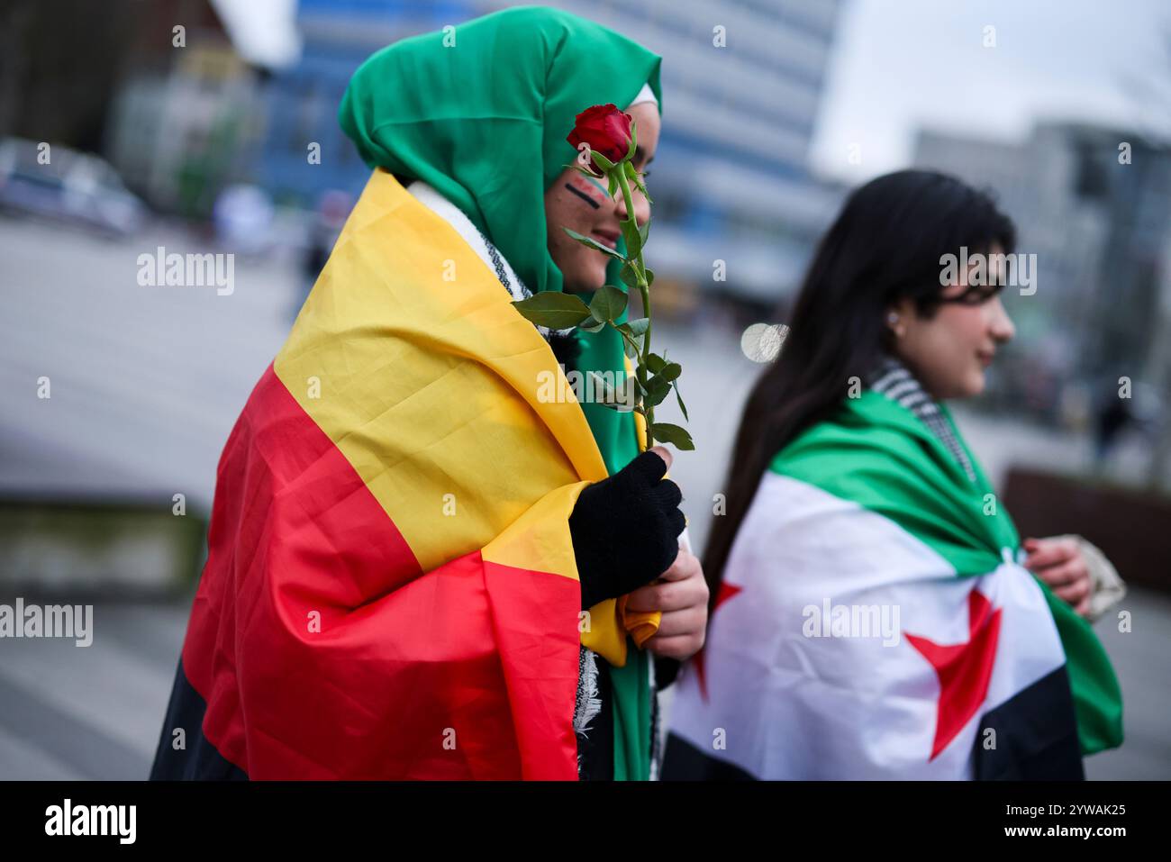 10 dicembre 2024, Renania settentrionale-Vestfalia, Duisburg: La diciottenne siriana Batuol Almussa (l) indossa la bandiera della rivoluzione siriana dipinta sul viso, una rosa tra le mani e la bandiera tedesca intorno alle spalle mentre celebra con la sua amica siriana Sara Shekho, che indossa la bandiera della rivoluzione siriana intorno alle sue spalle, di fronte alla stazione ferroviaria principale di Duisburg. I celebratori avevano mostrato bandiere della rivoluzione siriana e applaudito. La bandiera degli oppositori del regime di Assad mostra tre strisce orizzontali, una verde, una bianca e una nera, oltre a tre stelle rosse. Foto: Chr Foto Stock