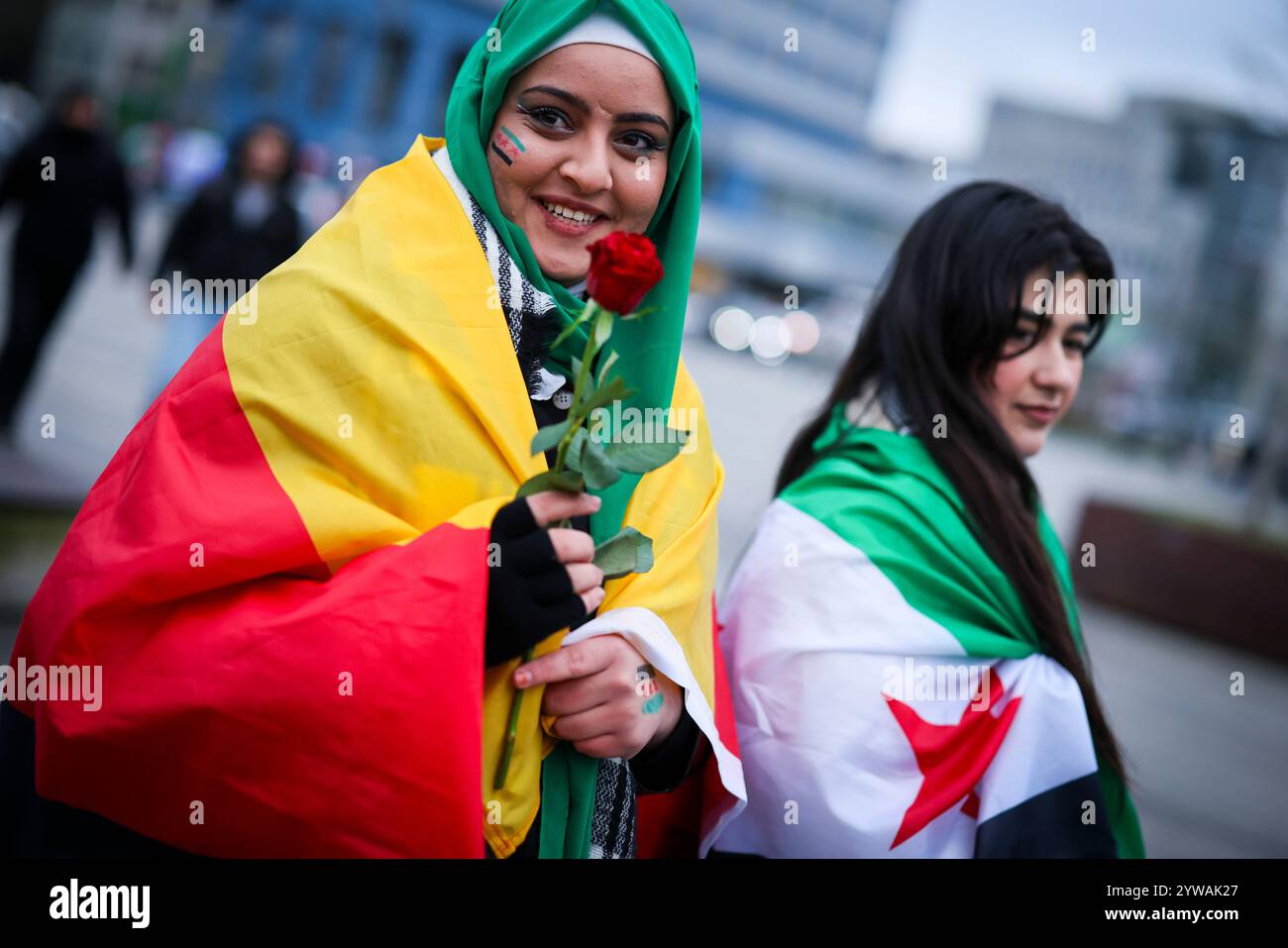 10 dicembre 2024, Renania settentrionale-Vestfalia, Duisburg: La diciottenne siriana Batuol Almussa (l) indossa la bandiera della rivoluzione siriana dipinta sul viso, una rosa tra le mani e la bandiera tedesca intorno alle spalle mentre celebra con la sua amica siriana Sara Shekho, che indossa la bandiera della rivoluzione siriana intorno alle sue spalle, di fronte alla stazione ferroviaria principale di Duisburg. I celebratori avevano mostrato bandiere della rivoluzione siriana e applaudito. La bandiera degli oppositori del regime di Assad mostra tre strisce orizzontali, una verde, una bianca e una nera, oltre a tre stelle rosse. Foto: Chr Foto Stock