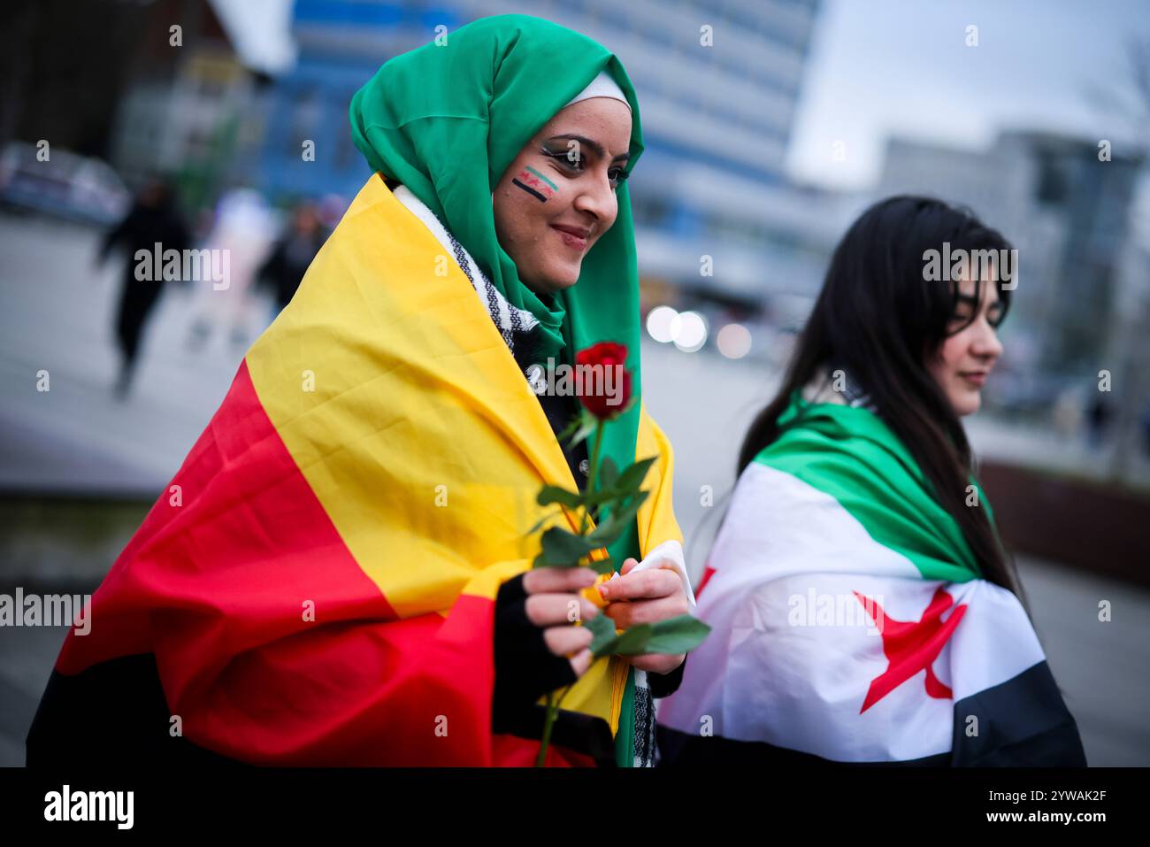 10 dicembre 2024, Renania settentrionale-Vestfalia, Duisburg: La diciottenne siriana Batuol Almussa (l) indossa la bandiera della rivoluzione siriana dipinta sul viso, una rosa tra le mani e la bandiera tedesca intorno alle spalle mentre celebra con la sua amica siriana Sara Shekho, che indossa la bandiera della rivoluzione siriana intorno alle sue spalle, di fronte alla stazione ferroviaria principale di Duisburg. I celebratori avevano mostrato bandiere della rivoluzione siriana e applaudito. La bandiera degli oppositori del regime di Assad mostra tre strisce orizzontali, una verde, una bianca e una nera, oltre a tre stelle rosse. Foto: Chr Foto Stock