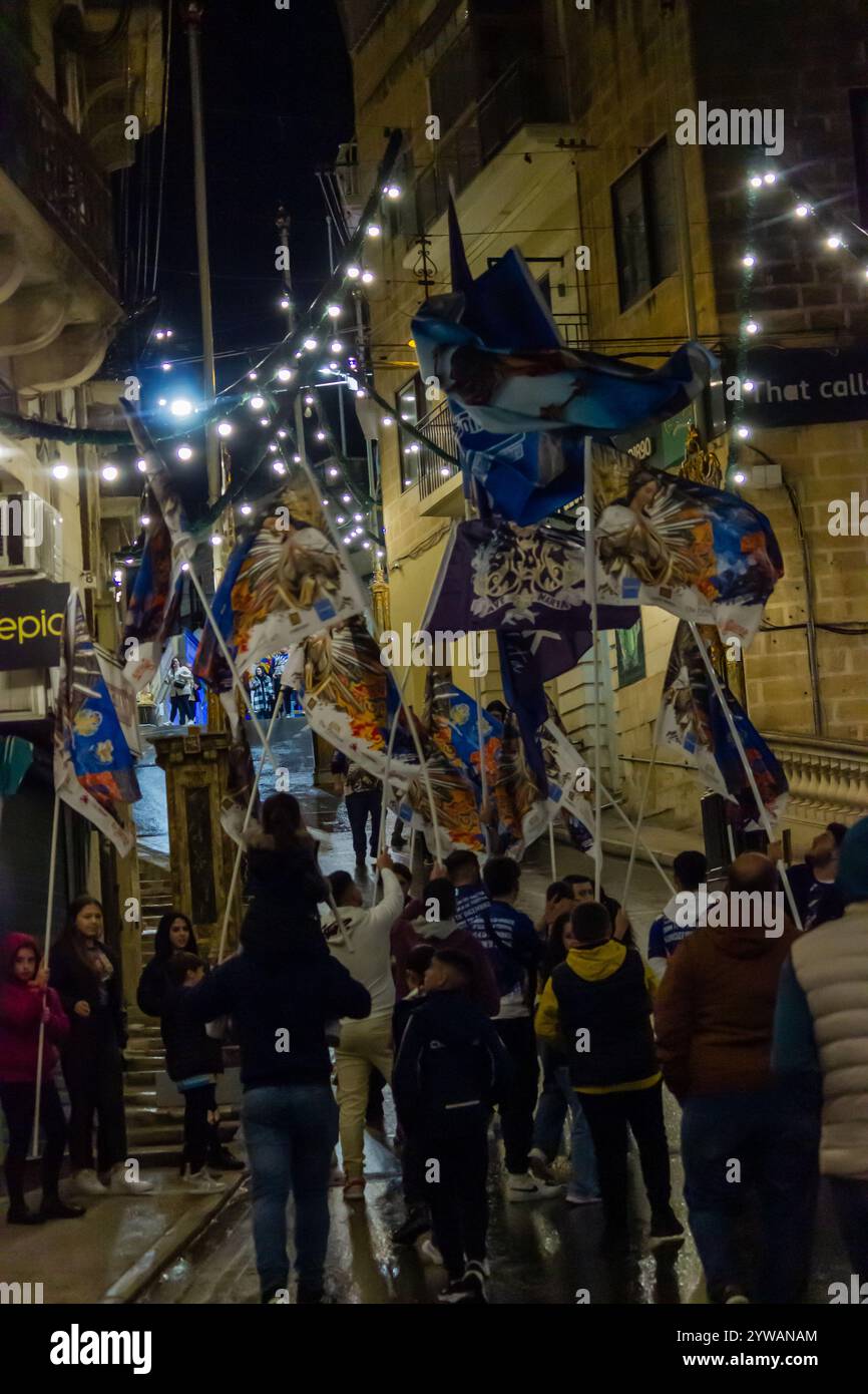 Cospicua, Malta - 6 dicembre 2024. Festa notturna eccitata con bandiere colorate e folla entusiasta Foto Stock