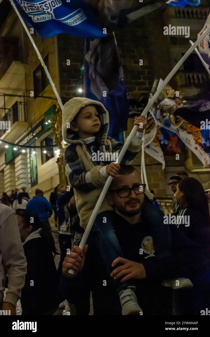 Cospicua, Malta - 6 dicembre 2024. Festa notturna eccitata con bandiere colorate e folla entusiasta Foto Stock